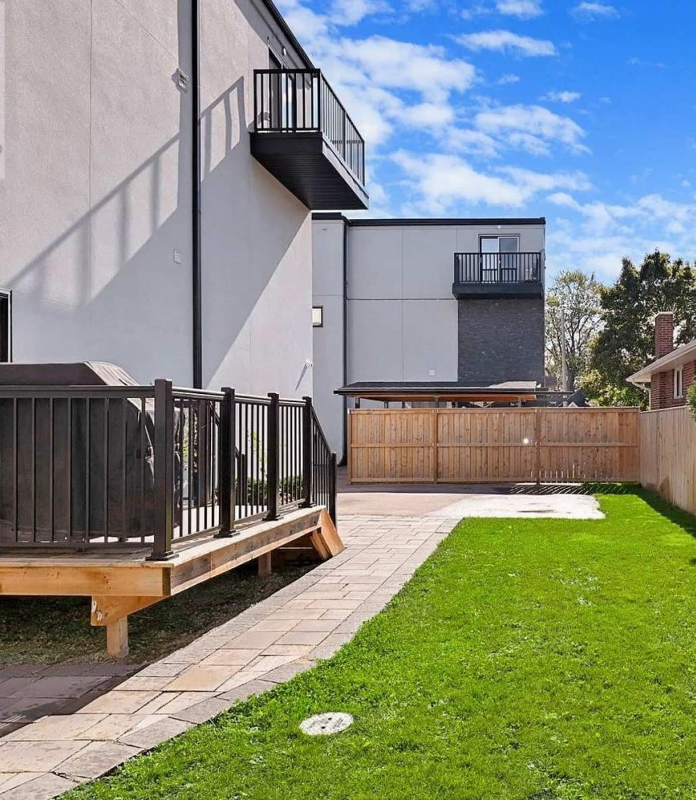 The private fenced backyard: a raised deck off the house, a paved path and patio, a lawn, and cedar fencing along the boundary
