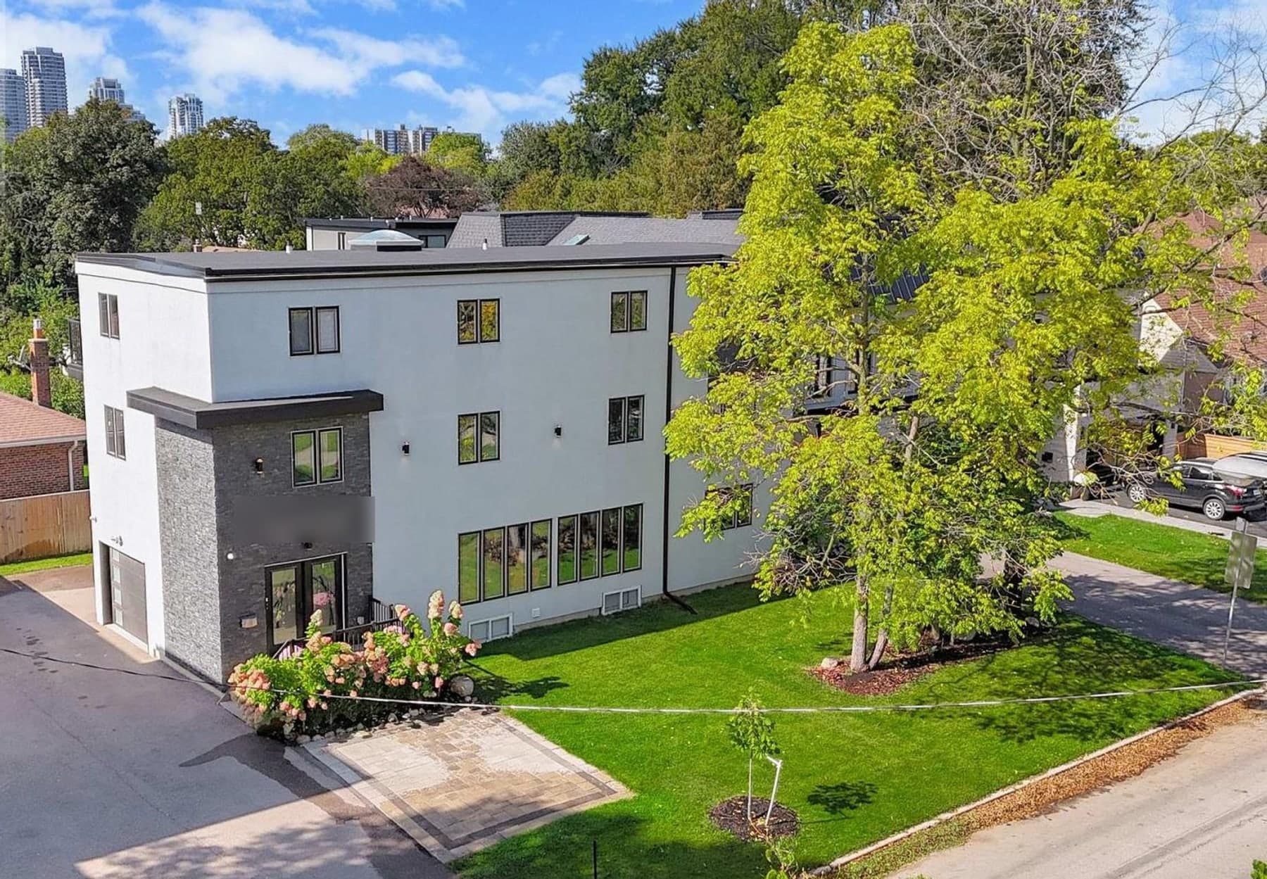 The Gatherwell home seen from above — a modern three-storey house in white render and stone, with a front lawn, mature trees, a private driveway and a quiet Etobicoke street
