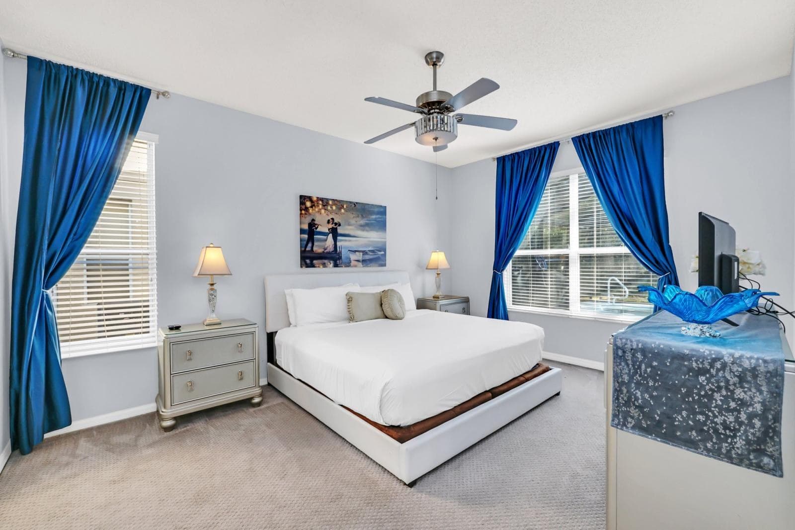 The ground-floor bedroom, with a large bed, a ceiling fan and a wave painting above the headboard