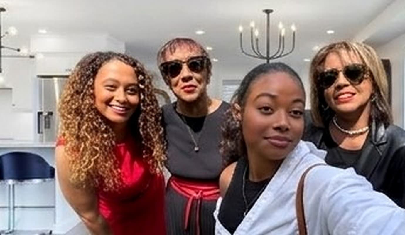 Four women of three generations of the same family, arm in arm in the kitchen at Gatherwell, the chandelier and the island behind them