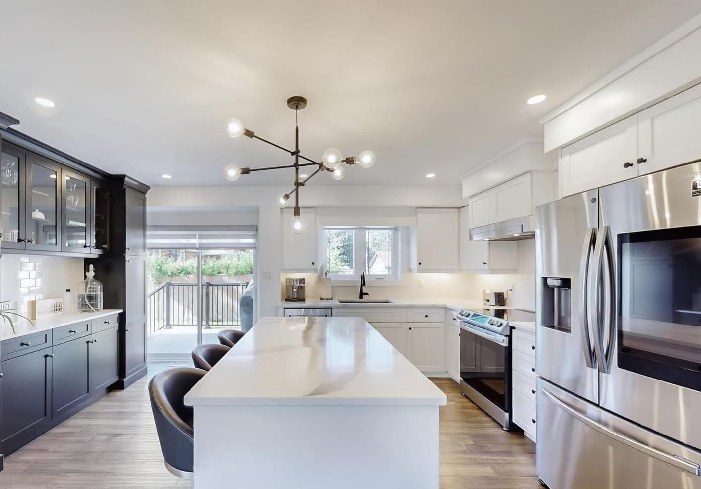 The main kitchen with a long quartz island, a range and full-size refrigerator, a window over the sink and doors out to the deck